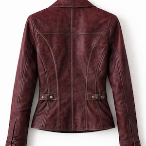 May include: A dark burgundy jacket with a distressed finish, featuring a collared neckline, long sleeves with buttoned cuffs, and adjustable side tabs with brass-toned hardware. The back panel includes vertical seam detailing and a structured fit.
