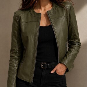 May include: An olive green jacket with a round neckline and a full-length front zipper. The jacket features long sleeves, horizontal seam detailing across the chest, and two vertical zippered pockets on the sides, worn over a black top and pants.