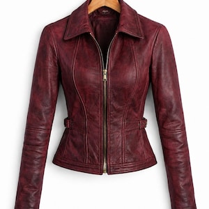 May include: A deep burgundy jacket with a distressed finish, featuring a pointed collar, long sleeves, and a central gold-toned zipper closure. The garment includes vertical seam detailing and adjustable side waist tabs with small buckles.