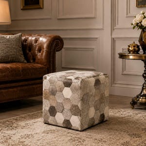 Puede incluir: Un taburete cuadrado con un patrón geométrico de parches hexagonales en varios tonos de gris, blanco y marrón. La superficie tiene una apariencia texturizada con un acabado de pelo corto, creando un diseño de panal repetitivo en los lados.