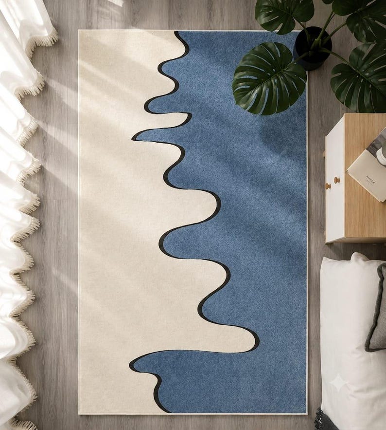 K&ouml;nnte beinhalten: Ein rechteckiger Teppich mit einem zweifarbigen Design, bestehend aus einem cremefarbenen und einem blauen Bereich, die durch eine markante, wellenf&ouml;rmige schwarze Linie getrennt sind, welche vertikal durch die Mitte verl&auml;uft.