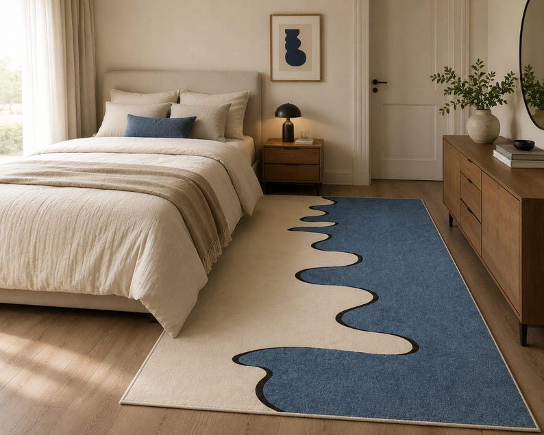 K&ouml;nnte beinhalten: Ein rechteckiger Teppich mit einem zweifarbigen Design, bestehend aus einem cremefarbenen Bereich und einem gro&szlig;en blauen Bereich, die durch eine kr&auml;ftige, schwarze, wellenf&ouml;rmige Linie getrennt sind, die ein flie&szlig;endes, abstraktes Muster bildet.