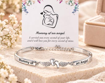 May include: A silver-toned metal bracelet featuring a central charm of two small feet with wings adorned with clear crystals. The bracelet is engraved with the text Mommy of an Angel and is displayed with a card featuring a line art illustration.
