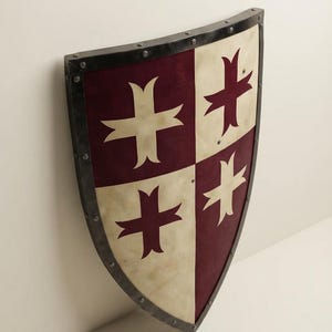 Może przedstawiać: Tarcza herbowa o ćwiartkowym wzorze z naprzemiennymi sekcjami w kolorze bordowym i złamanej bieli. Każda sekcja zawiera stylizowany emblemat krzyża w kontrastującym kolorze. Tarcza jest obramowana ciemną metalową krawędzią z widocznymi nitami.