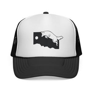 Peut inclure: Une casquette trucker blanche et noire avec une impression graphique sur le panneau avant. Le motif présente une forme rectangulaire noire unie avec un bord inférieur dentelé, un petit cercle blanc et le contour blanc d'un renard sautant.