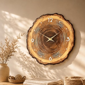 May include: A round wall clock made from a natural wood slice with visible tree rings, featuring white numerals at 12, 3, 6, and 9 o'clock, and thin gold-coloured metal hands. The clock face displays a dark brown centre with lighter wood edges.