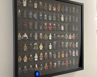 Könnte beinhalten: Eine schwarze rechteckige Vitrine mit Glasfront, die eine Sammlung zahlreicher kleiner Kunststofffiguren in Reihen enthält. Die Figuren weisen verschiedene Farben und Designs auf, und unten befindet sich ein kleines kreisförmiges blaues Licht.