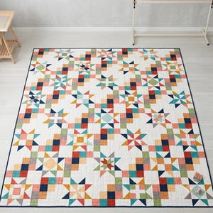 May include: A rectangular quilt featuring a repeating pattern of multi-colored stars and small square blocks on a white background. The design incorporates shades of navy blue, teal, coral, yellow, and green, finished with a dark blue border.