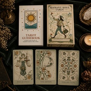 May include: The Radiant Soul Tarot deck box and guidebook are displayed alongside three tarot cards: The Justice, The Moon, and Ten of Cups. The box features an illustration of a person walking with a flower, while the guidebook shows a sun icon.