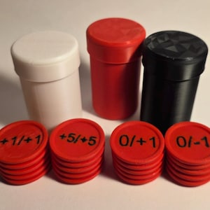 Puede incluir: Tres recipientes cilíndricos en blanco, rojo y negro, acompañados de cuatro pilas de fichas circulares rojas. Las fichas están marcadas con texto negro que dice +1/+1, +5/+5, 0/+1 y 0/-1. Los recipientes tienen tapas, la negra presenta una textura geométrica facetada.