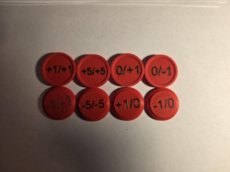 May include: Eight circular red plastic tokens arranged in two rows of four. Each token features black printed text displaying various numerical values including +1/+1, +5/+5, 0/+1, 0/-1, -1/-1, -5/-5, +1/0, and -1/0, with a raised border edge.