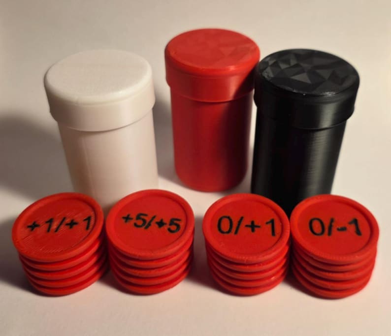 May include: Three cylindrical containers in white, red, and black, accompanied by four stacks of red circular tokens. The tokens are marked with black text reading +1/+1, +5/+5, 0/+1, and 0/-1. The containers have lids, with the black lid featuring a geometric faceted texture.