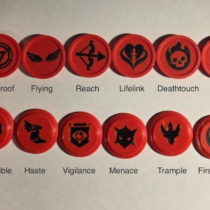 May include: Twelve circular red tokens with black icons representing game abilities. The top row features Hexproof, Flying, Reach, Lifelink, Deathtouch, and Double Strike. The bottom row displays Indestructible, Haste, Vigilance, Menace, Trample, and First Strike.