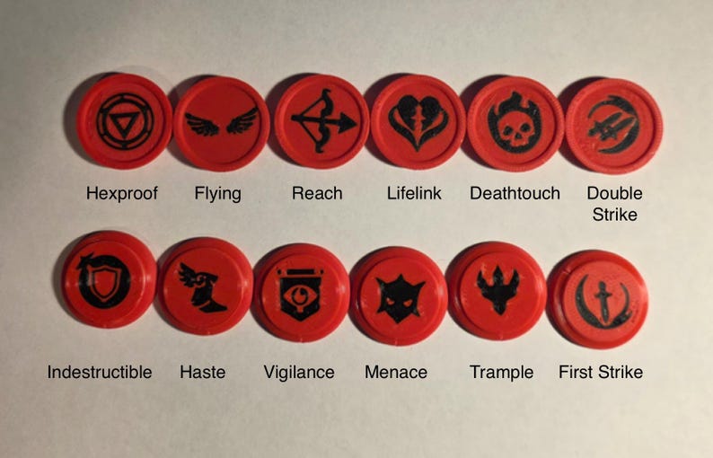 May include: Twelve circular red tokens with black icons representing game abilities. The top row features Hexproof, Flying, Reach, Lifelink, Deathtouch, and Double Strike. The bottom row displays Indestructible, Haste, Vigilance, Menace, Trample, and First Strike.