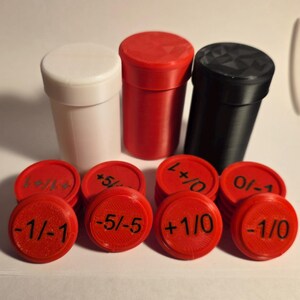 May include: Three cylindrical containers in white, red, and black, accompanied by a collection of red circular tokens. Each token features black printed numerical values including -1/-1, -5/-5, +1/0, 0/-1, and +1/+1, designed for game tracking.