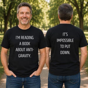 Puede incluir: Una camiseta negra de manga corta con texto en blanco. El frente dice I'M READING A BOOK ABOUT ANTI-GRAVITY. La parte posterior dice IT'S IMPOSSIBLE TO PUT DOWN. La camiseta se combina con pantalones vaqueros azules, mostrando la parte frontal y trasera.