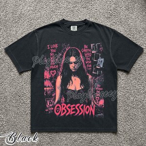 May include: A black short-sleeve t-shirt featuring a pink graphic print of a person with long dark hair. The text reads I LOVE YOU SO SO SO SO MUCH, BE CAREFUL WHO YOU WISH FOR, YOU WISHED FOR THIS, and OBSESSION, accompanied by heart icons.