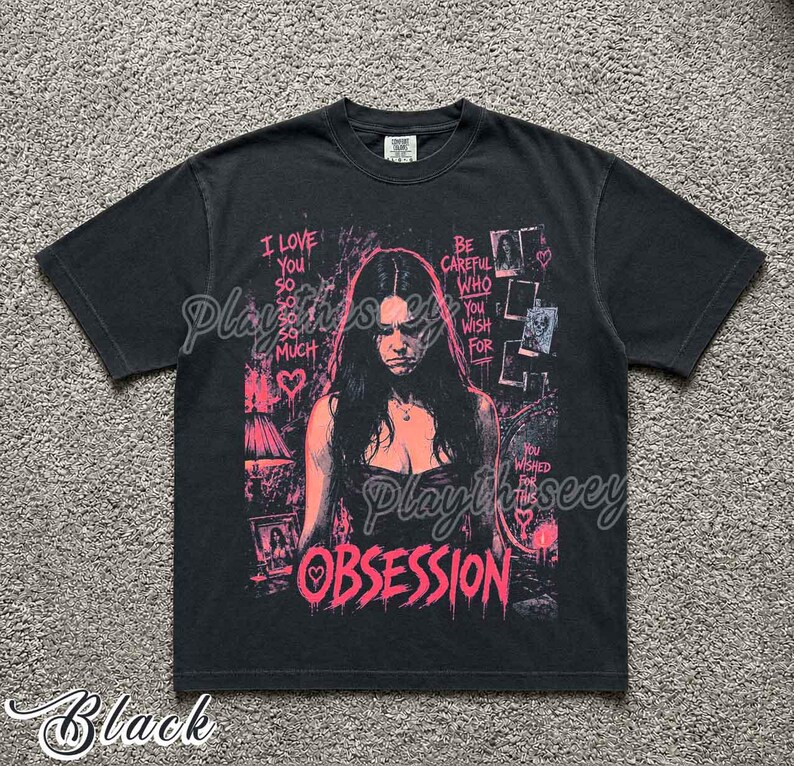 May include: A black short-sleeve t-shirt featuring a pink graphic print of a person with long dark hair. The text reads I LOVE YOU SO SO SO SO MUCH, BE CAREFUL WHO YOU WISH FOR, YOU WISHED FOR THIS, and OBSESSION, accompanied by heart icons.