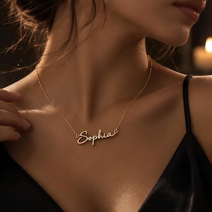 May include: A gold-toned metal necklace featuring a delicate chain and a central nameplate pendant displaying the name Sophia in a cursive, flowing script font. The pendant is attached to the chain at both ends, creating a centered, horizontal display.