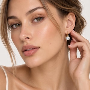 May include: A gold hoop earring featuring a small, oval-shaped clear gemstone pendant. The earring is crafted from polished yellow gold metal, with the clear stone securely set in a matching gold bezel, creating a simple and refined jewelry piece.
