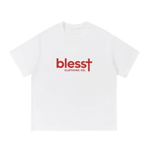 May include: A white short-sleeved t-shirt featuring a red graphic on the chest. The graphic displays the word "blesst" in a lowercase sans-serif font, with the letter "t" stylized as a cross, and the text "CLOTHING CO." printed underneath.