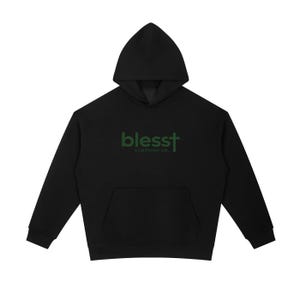 May include: A black hooded sweatshirt featuring long sleeves, a front kangaroo pocket, and a hood. The chest displays the dark green text "blesst" with a cross replacing the letter "t", followed by the smaller text "CLOTHING CO." underneath.