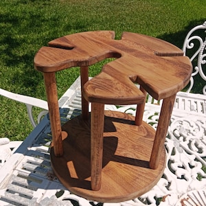 May include: A circular wooden stand featuring a smooth, polished brown finish with a distinct grain pattern. The structure consists of a solid base supported by four cylindrical legs, topped with a platform containing four cut-out slots.