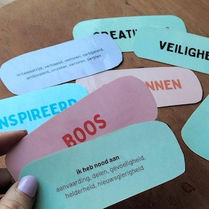 Op de afbeelding: Een verzameling rechthoekige kaarten met afgeronde hoeken in pastelkleuren zoals lichtblauw, roze en mintgroen. De kaarten bevatten gedrukte Nederlandse tekst zoals 'BOOS', 'INSPIREERD', 'VEILIGHEID' en 'CREATIVITEIT', samen met beschrijvende lijsten van emoties.