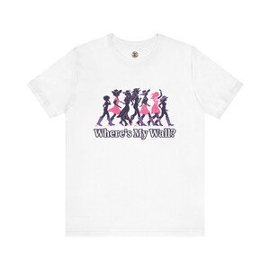 Könnte beinhalten: Ein weißes Kurzarm-T-Shirt mit einer Grafik von sieben Silhouetten, die in einer Reihe gehen und Hüte sowie Stiefel in Rosa- und Violetttönen tragen. Unter den Figuren ist der Text "Where's My Wall?" in dunkelvioletter Schrift aufgedruckt.