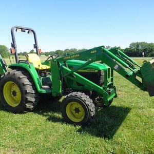 Puede incluir: Un tractor John Deere 4600 de color verde con un cargador frontal 460 y una retroexcavadora trasera. El tractor cuenta con un asiento amarillo, una estructura de protección antivuelco negra y neumáticos grandes de caucho negro.