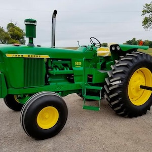 May include: A green John Deere 5020 diesel tractor featuring yellow wheels, a black exhaust pipe, a vertical air intake, and a yellow seat. The tractor has large rear tires with deep treads and smaller front tires, with a metal ladder on the side.