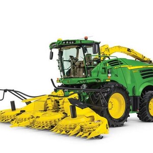 Puede incluir: Una cosechadora de forraje autopropulsada John Deere 8600 de color verde y amarillo con un cabezal rotativo frontal grande de varios discos de corte, una cabina de operador elevada, neumáticos negros grandes y un tubo de descarga amarillo.