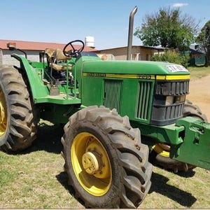 Könnte beinhalten: Ein grüner John Deere 6205 Traktor mit großen schwarzen Reifen, gelben Felgen und einem an der Vorderseite montierten Gewichtblock. Das Fahrzeug verfügt über ein schwarzes Lenkrad, einen offenen Fahrerstand und ein vertikales Auspuffrohr.