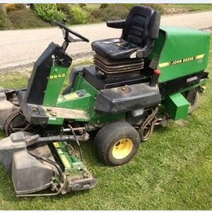 Peut inclure: Une tondeuse autoportée diesel John Deere 2243 verte et noire avec un siège conducteur noir, un volant et des unités de coupe montées à l'avant. La machine possède des moyeux de roue jaunes et affiche le logo John Deere et le numéro 2243.
