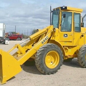 Puede incluir: Una cargadora de ruedas amarilla John Deere 444C con un gran cucharón frontal, una cabina de operador totalmente cerrada con ventanas de cristal y cuatro neumáticos de goma resistentes. El número 444C está impreso en el brazo de carga.