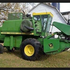 Puede incluir: Una cosechadora John Deere 4400 de color verde y amarillo con un accesorio de corte 213. La máquina agrícola cuenta con una cabina cerrada grande, neumáticos negros resistentes con llantas amarillas y marcas visibles en los paneles laterales.