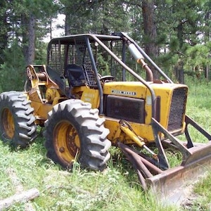 Peut inclure: Un débardeur John Deere jaune doté d'une cage de protection noire, de gros pneus à crampons robustes et d'une lame métallique montée à l'avant. Le véhicule forestier industriel est positionné dans une zone herbeuse avec une forêt en arrière-plan.
