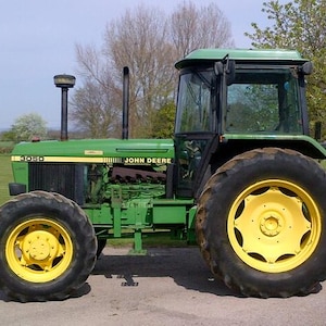 Puede incluir: Un tractor John Deere 3050 de color verde con neumáticos negros grandes y llantas amarillas. El vehículo cuenta con una cabina acristalada, un tubo de escape negro alto y una rejilla frontal negra. El número de modelo 3050 aparece en el capó.
