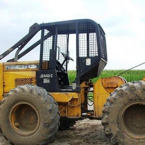 Può includere: Un esboscatore John Deere JD440-C giallo dotato di una gabbia protettiva nera con rete, grandi pneumatici in gomma per impieghi gravosi e un volante visibile all'interno della cabina aperta. Il veicolo forestale industriale ha un telaio in metallo.