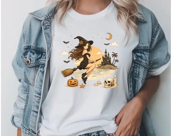 May include: A white t-shirt featuring a graphic illustration of a witch with long brown hair wearing a black dress and hat, flying on a broomstick over a beach with a castle, a crescent moon, bats, a pumpkin, a starfish, and a skull.
