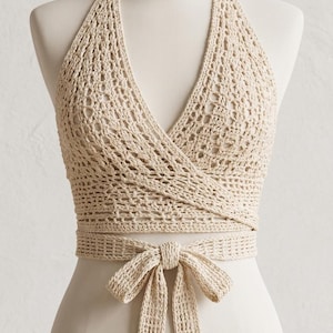 May include: A beige crochet halter top featuring a deep V-neckline with a wrap-around design that ties at the waist. The garment is crafted with an openwork stitch pattern and includes a small reference image in the corner showing multiple ways to wear.