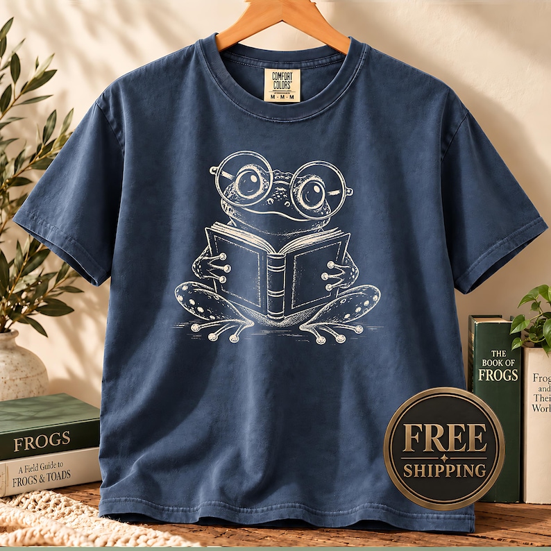 Cute frog shirt featuring a hand sketched frog with big round glasses reading a book, cute frog shirt for readers, book club sweatshirt, book lover shirt, reading shirt, frog reading shirt, bookish shirt, book club shirt, library shirt, book lover gift, frog lover gift, frog sweatshirt, bookish sweatshirt, comfort colors shirt, cute bookish frog tee, reading lover gift, bookworm shirt, librarian gift, frog gift for readers