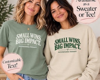 May include: A sage green t-shirt and a beige sweatshirt, both featuring the dark green text "SMALL WINS. BIG IMPACT." and "OCCUPATIONAL THERAPY" with a small heart graphic. The image includes text overlays stating "Available as a Sweater or Tee!" and "Customizable Text!"