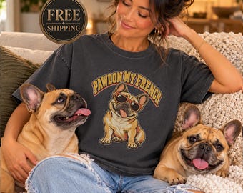 May include: A charcoal gray short-sleeve t-shirt featuring a graphic of a tan French Bulldog wearing red sunglasses with its tongue out. The text above the dog reads "PAWDON MY FRENCH" in a bold, arched, yellow and orange retro-style font.