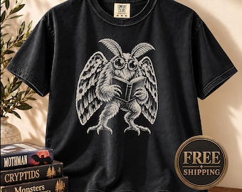 May include: A black short-sleeve t-shirt featuring a white graphic illustration of a moth-like creature wearing round glasses and reading an open book. The shirt has a crew neckline and a Comfort Colors brand label printed on the inside collar.