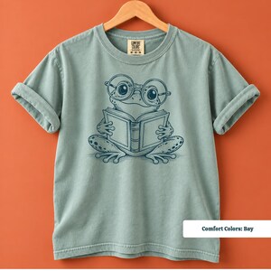 Frog lover gift with a cute hand drawn frog in oversized round eyeglasses holding and reading an open book, cute frog shirt, book club sweatshirt, book lover shirt, reading shirt, frog reading shirt, bookish shirt, book club shirt, library shirt, book lover gift, frog sweatshirt, bookish sweatshirt, comfort colors shirt, frog lover shirt, bookworm gift, reader gift, reading gift, librarian gift, cute bookish tee, frog gift