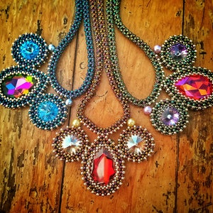 Könnte beinhalten: Drei Perlenketten mit bunten Kristallanhängern. Die Ketten sind aus kleinen, schillernden Perlen gefertigt und haben Kristalle in verschiedenen Farben, darunter Rot, Blau und Lila.