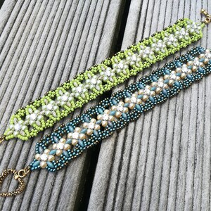 May include: Two beaded bracelets with heart-shaped clasps. One bracelet is green with white beads, the other is blue with white and gold beads.