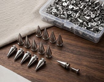 May include: A collection of silver-colored metal cone-shaped spikes with threaded screw backs. Several spikes are arranged in rows on a wooden surface, while a large quantity of identical spikes is contained within a clear plastic storage box.