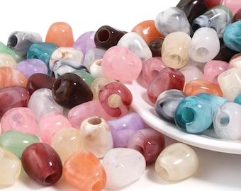 May include: A large collection of smooth, barrel-shaped beads in a variety of marbled and solid colors, including shades of pink, blue, white, brown, and orange. Each bead features a central hole, and many are piled on a white surface.